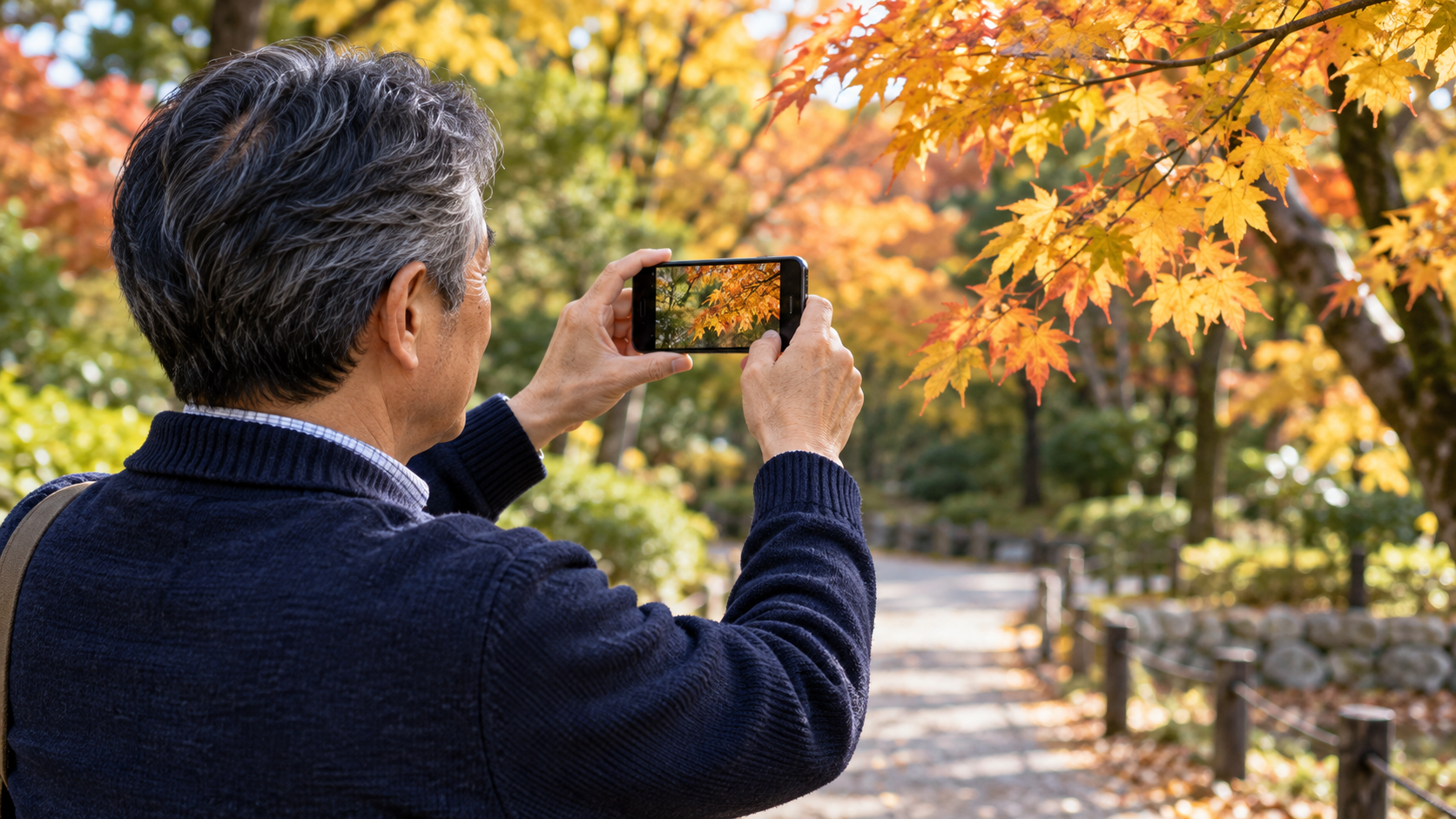公園で立ち止まり、秋の葉をスマートフォンで撮影する男性のイメージ